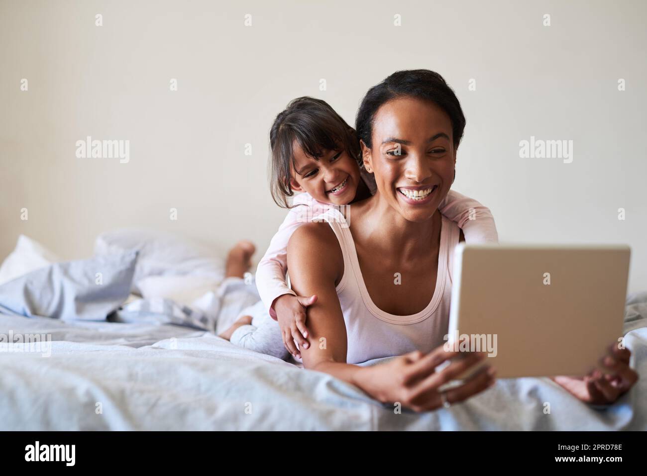 Mal sehen, was heute in der Welt im Trend ist. Eine schöne junge Mutter und Tochter mit einem digitalen Tablet, während sie sich zu Hause im Bett entspannen. Stockfoto