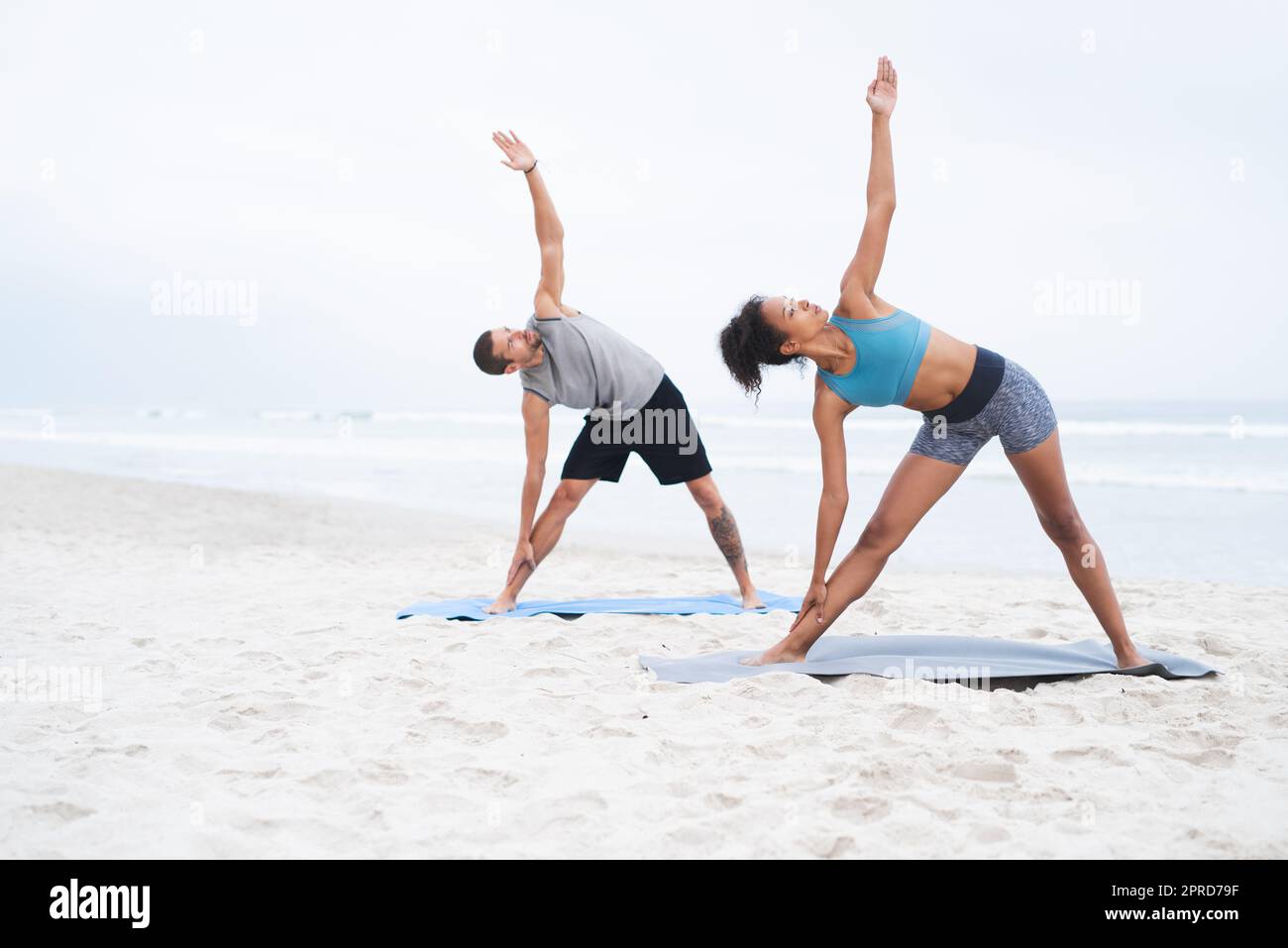 Yoga steht im Mittelpunkt ihres Wohlbefindens. Ein junger Mann und eine junge Frau praktizieren gemeinsam am Strand Yoga. Stockfoto