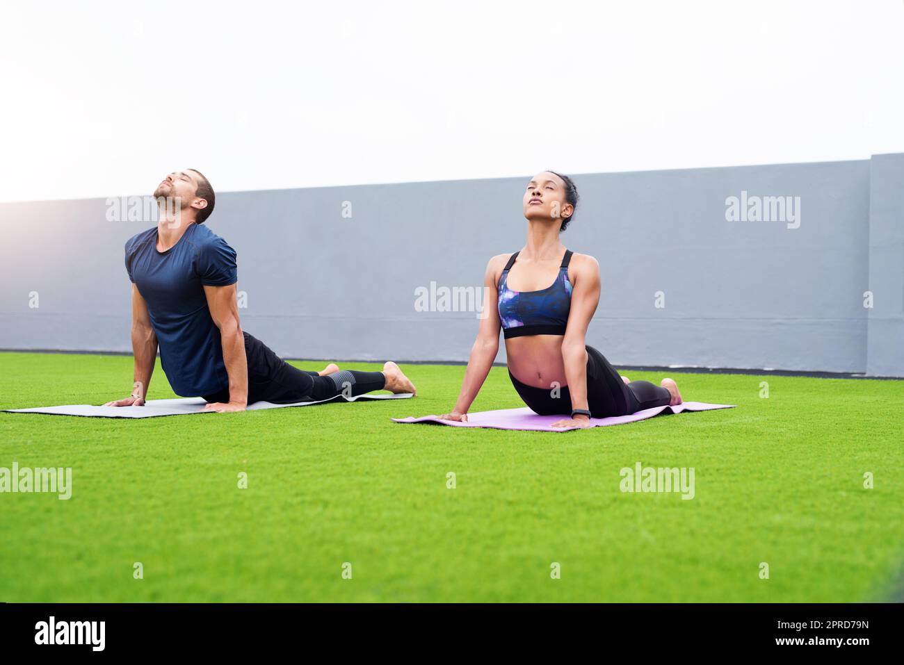 Ein junger Mann und eine junge Frau üben gemeinsam im Freien Yoga. Stockfoto