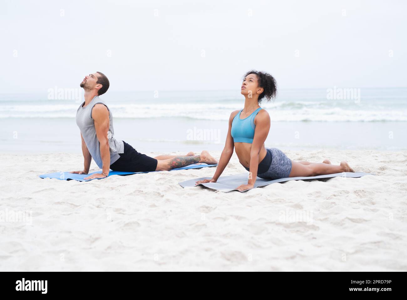Lassen Sie die ruhige Luft Ihren Körper und Geist erfüllen. Ein junger Mann und eine junge Frau üben gemeinsam am Strand Yoga. Stockfoto
