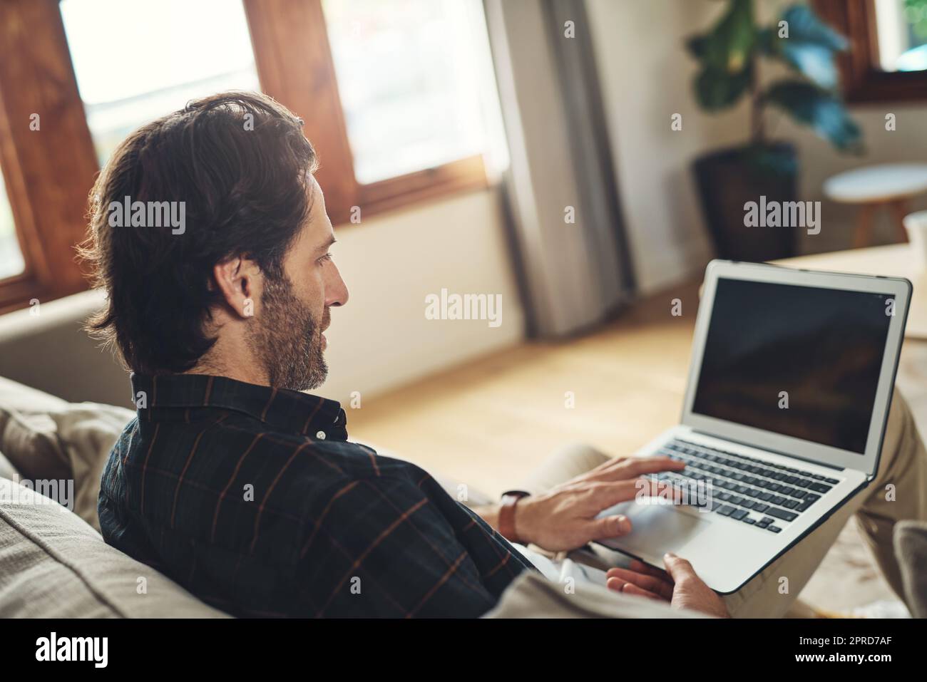 Lassen Sie uns herausfinden, was heute online Trend. Ein hübscher junger Mann mit seinem Laptop, während er sich auf einer Couch zu Hause entspannen. Stockfoto