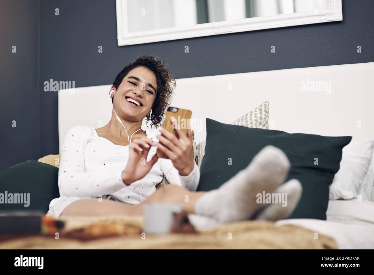 Eine schöne Frau, die Musik genießt, während sie ihr Telefon zu Hause im Bett benutzt. Stockfoto