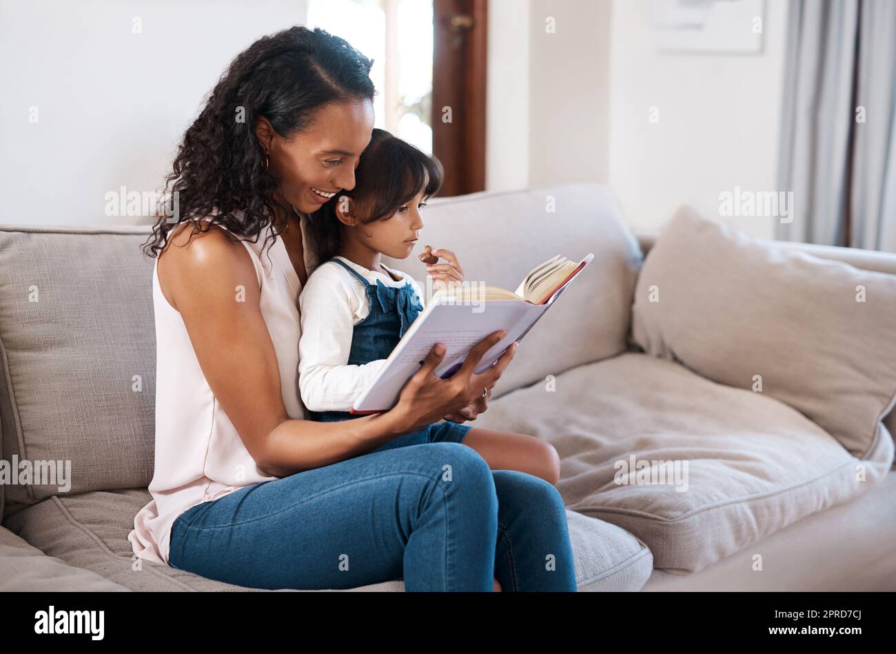 Bonding Time beinhaltet das Lesen unserer Lieblingsbücher. Ein junges Mädchen, das ein Buch liest, während es mit ihrer Mutter zu Hause sitzt. Stockfoto