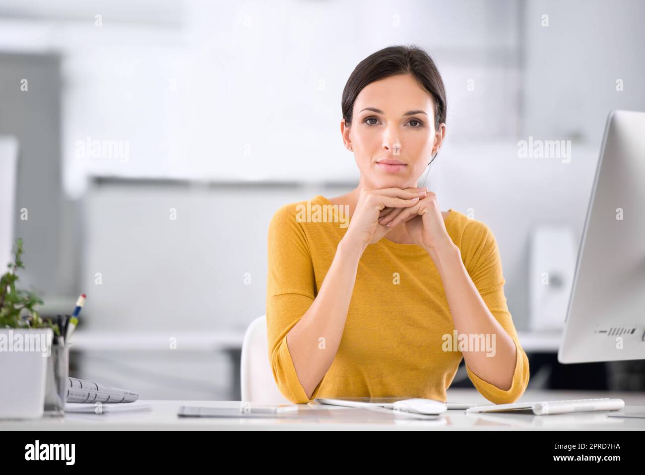 Seriöse, selbstbewusste und ehrgeizige Geschäftsfrau, die an ihrem Schreibtisch sitzt und ihr Kinn auf den Händen ruht. Porträt einer Unternehmerin, die während der Arbeit in einem Büro hervorragende Führungsqualitäten zeigt Stockfoto