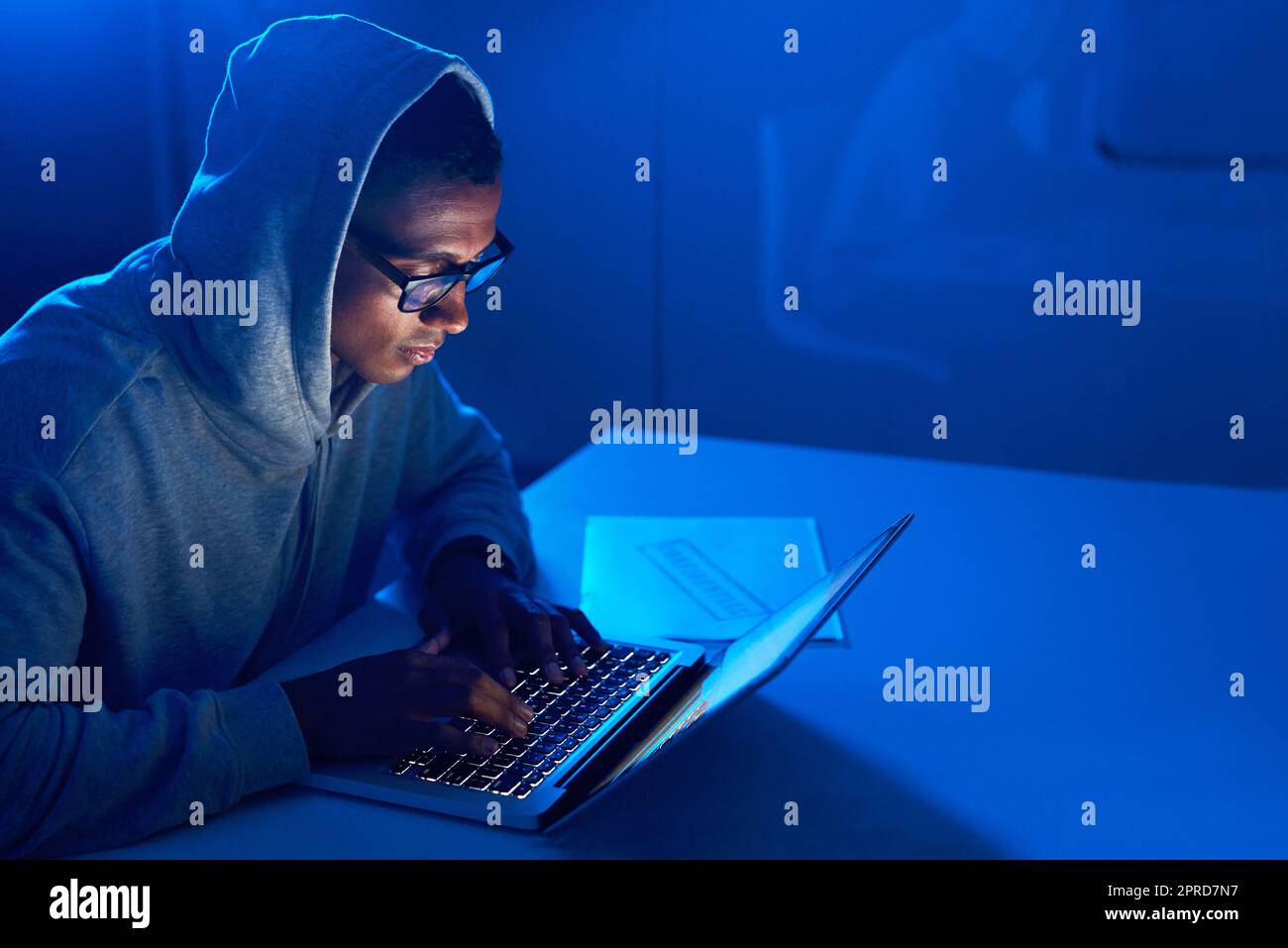 Ein junger männlicher Hacker mit einem Laptop im Dunkeln. Stockfoto