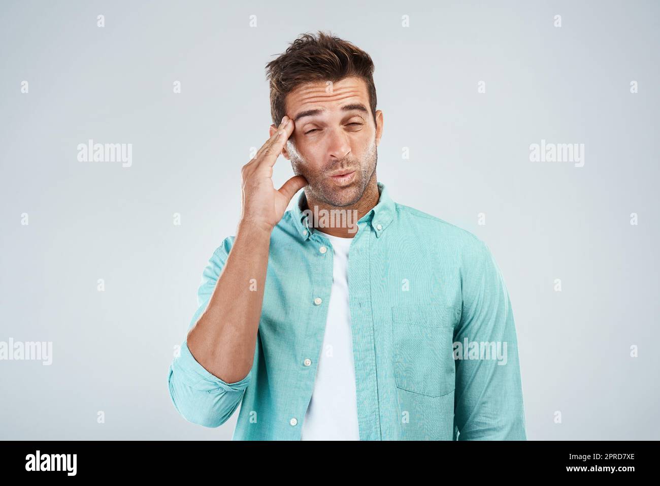 Wo kommt das her? Studioaufnahme eines jungen Mannes mit unangenehmem Gesichtsausdruck aufgrund von Kopfschmerzen, während er vor einem grauen Hintergrund steht. Stockfoto