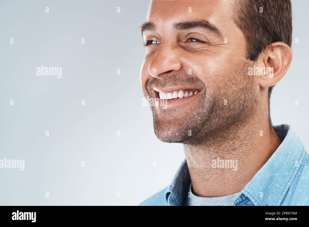 Ein fröhlicher junger Mann, der vor grauem Hintergrund lächelt und fröhlich lächelt. Stockfoto