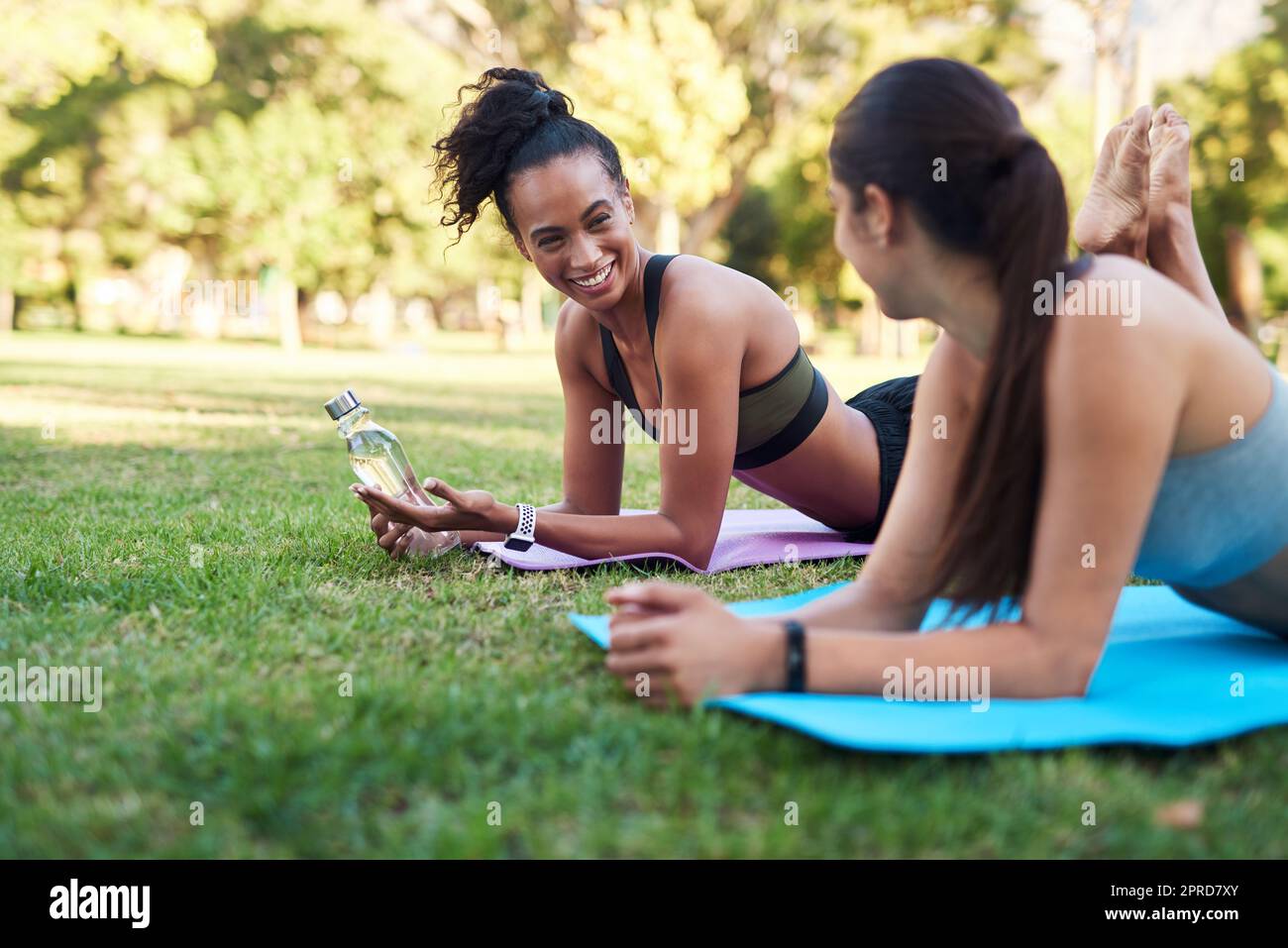 Zwei attraktive junge Frauen, die sich tagsüber im Park nebeneinander strecken. Stockfoto