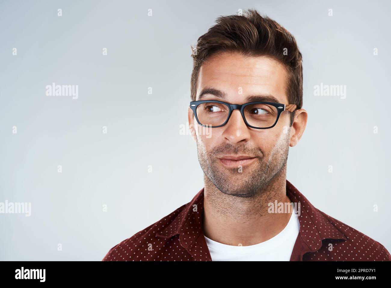 Seien Sie nicht schüchtern. Porträt eines fröhlichen jungen Mannes, der eine Brille trägt und hell lächelt, während er vor einem grauen Hintergrund steht. Stockfoto