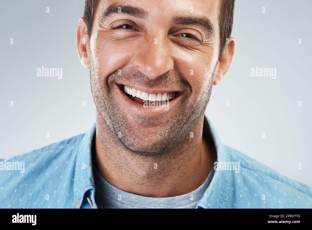 Nun, das ist ein gutes Lächeln. Porträt eines fröhlichen jungen Mannes, der hell lächelt und vor einem grauen Hintergrund steht. Stockfoto