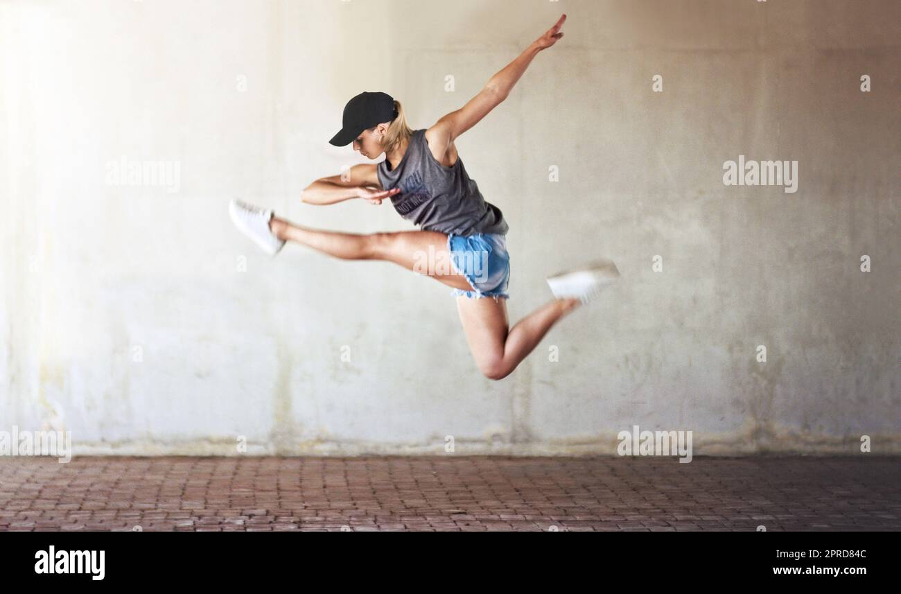 Im Tanz auf neue Höhen springen. In voller Länge eine attraktive junge Frau, die im Rahmen einer Tanzroutine springt und eine halbe Teilung macht. Stockfoto
