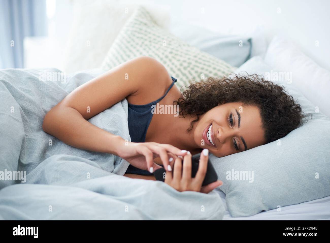 Das ist so ein lustiger Text. Eine attraktive junge Frau, die auf ihrer Seite im Bett liegt und morgens ihr Handy benutzt. Stockfoto