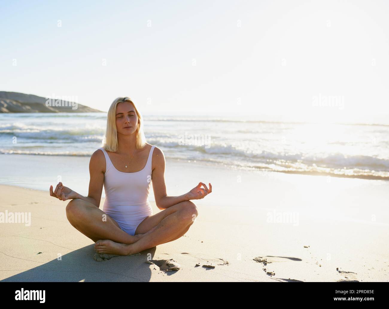 Am besten am Morgen ist es, mich auf den Atem zu konzentrieren. Ganzkörperaufnahme einer attraktiven jungen Frau, die mit gekreuzten Beinen am Strand sitzt und meditiert. Stockfoto