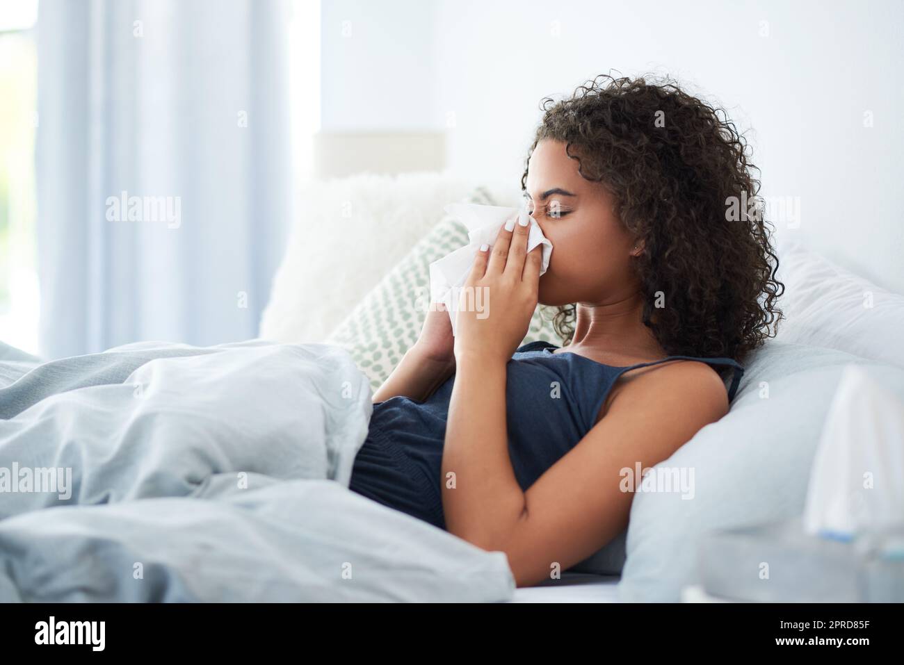 Oh nein, ich bekam eine Erkältung. Eine attraktive junge Frau, die sich krank fühlt und ihre Nase bläst, während sie morgens im Bett war. Stockfoto
