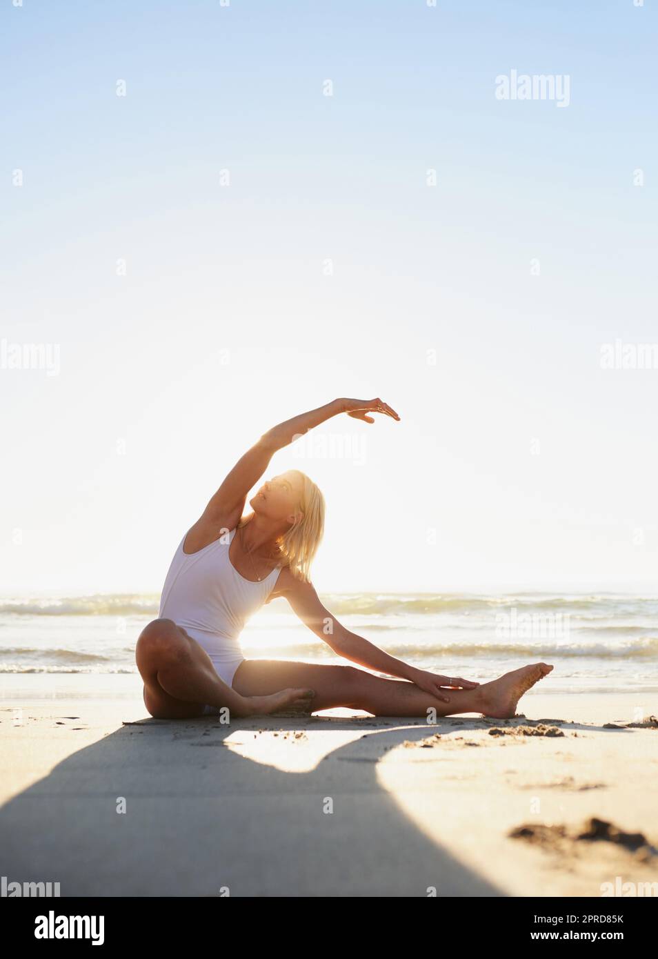 Achtet darauf, wie sich mein Körper anfühlt. In voller Länge eine attraktive junge Frau, die am frühen Morgen am Strand eine Yoga-Strecke macht. Stockfoto