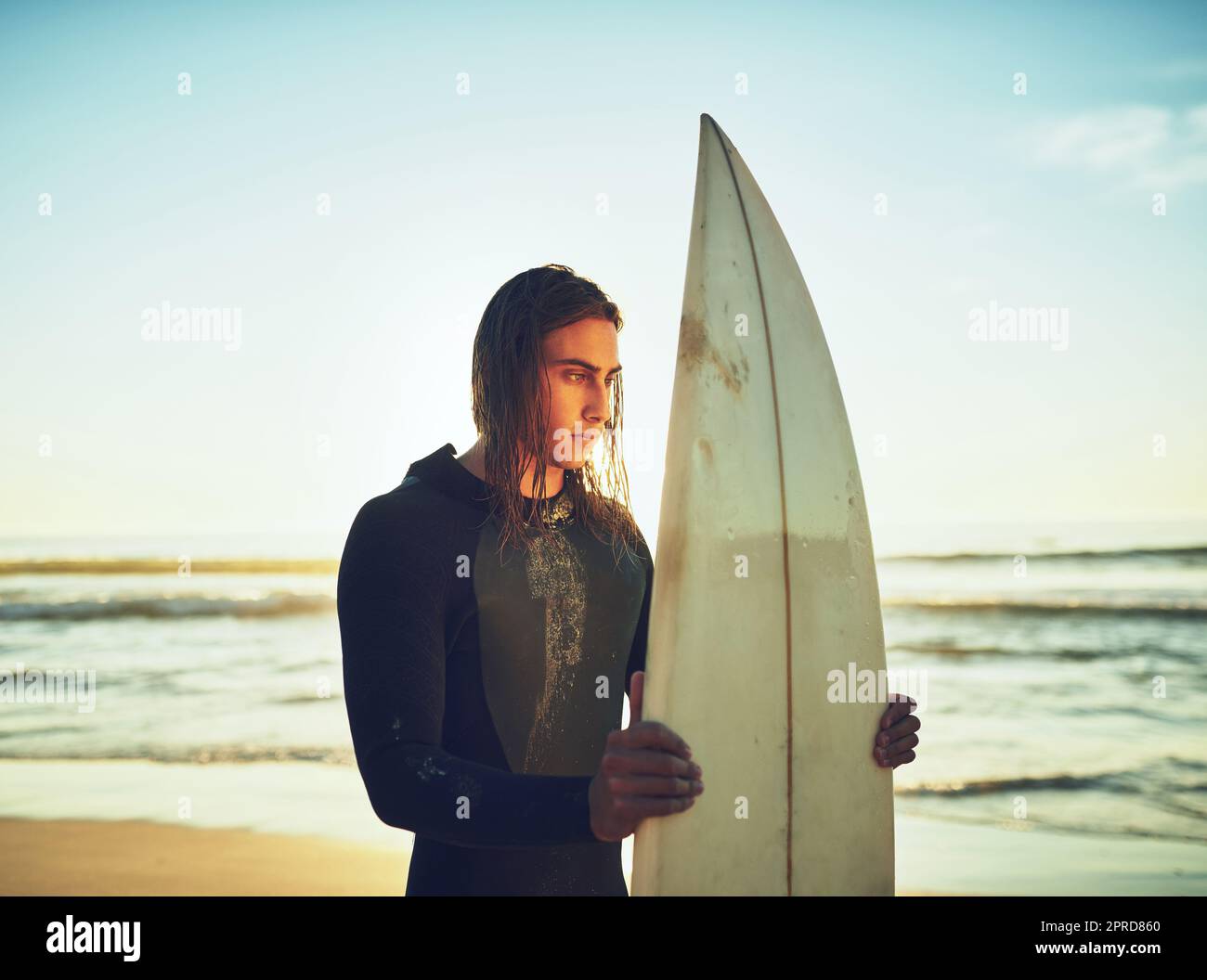 Ein junger Mann, der mit einem Surfbrett am Strand steht. Stockfoto