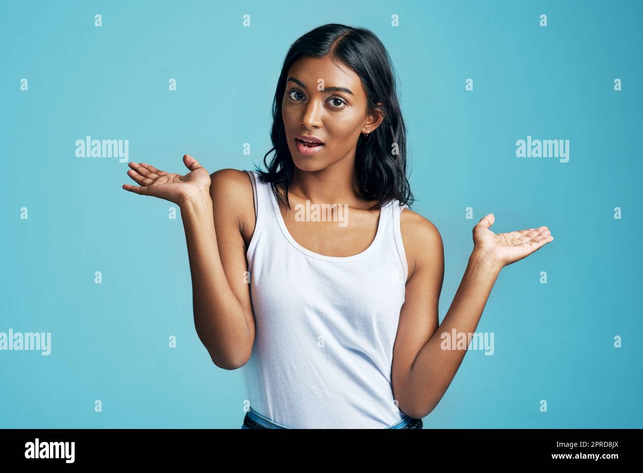 Schlägt mich. Studioporträt einer schönen jungen Frau, die ihre Schultern vor blauem Hintergrund zuckt. Stockfoto