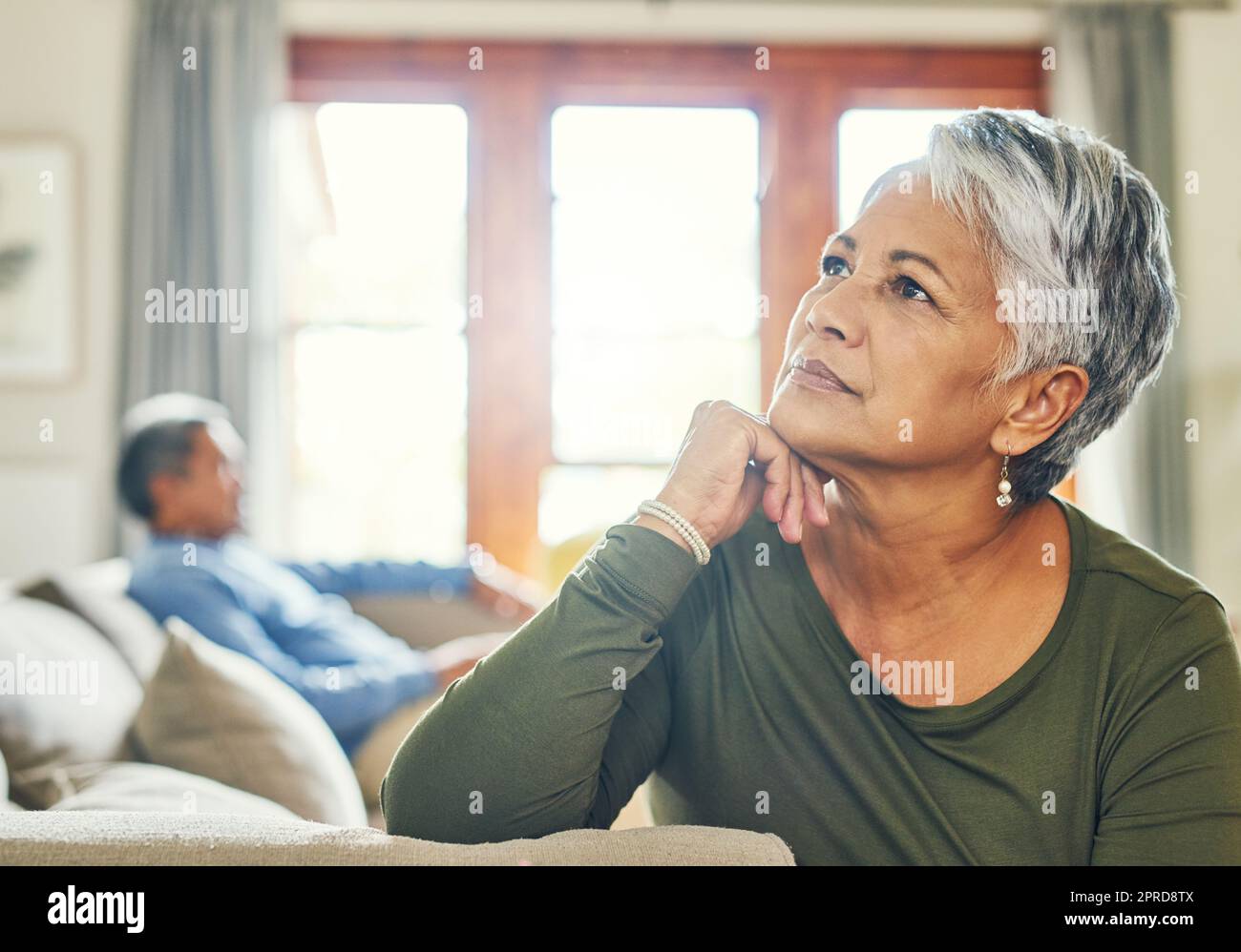 Er hat heute kein einziges Wort von mir bekommen. Eine wunderschöne Seniorin, die auf einer Couch sitzt und im Hintergrund mit ihrem Mann sehr aufmerksam aussieht. Stockfoto