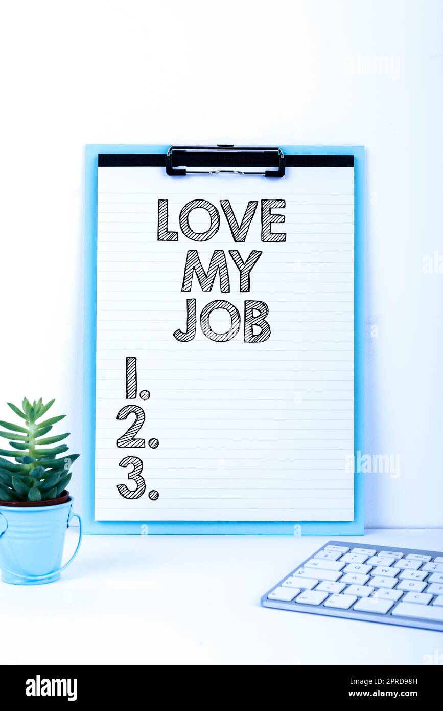 Handschrifttext „Love My Job“ (Mein Job lieben). Ein Wort, das geschrieben wurde, um sich über die Arbeit zu freuen, dass man sich wohlfühlt wichtige Nachricht, die auf der Zwischenablage am Schreibtisch mit Blume und Tastatur präsentiert wird. Stockfoto