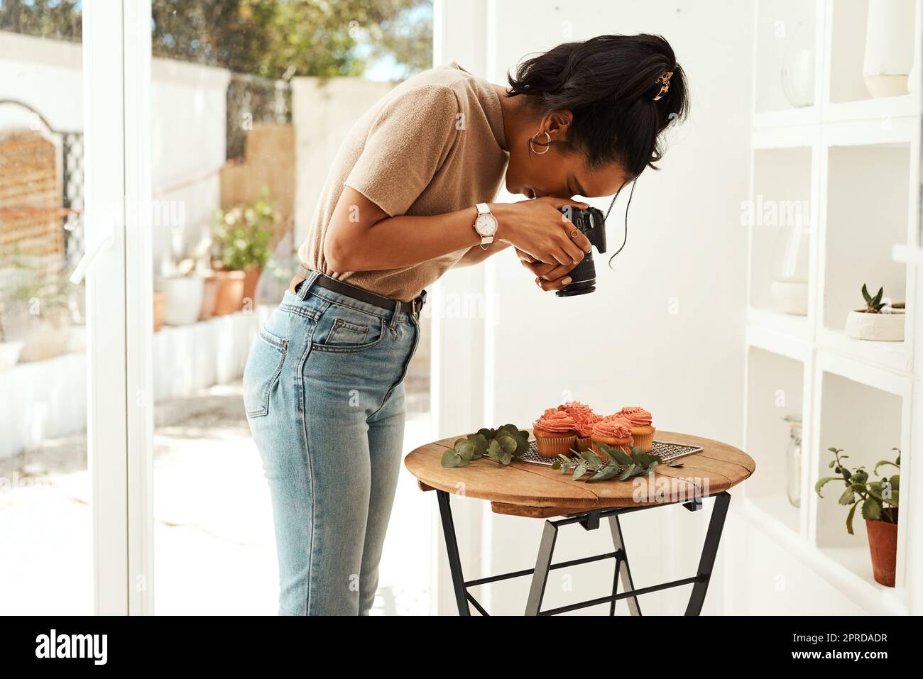 Das Zuckerguss sieht durch das Objektiv erstaunlich aus. Eine attraktive junge Geschäftsfrau steht und fotografiert mit ihrer Kamera Cupcakes für ihren Blog. Stockfoto