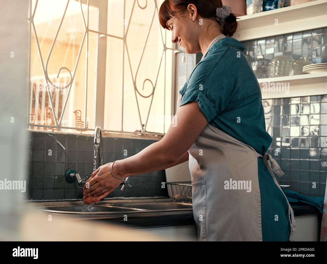 Halten Sie Ihre Hände immer keimfrei. Eine attraktive junge Frau, die sich in ihrer Küche zu Hause die Hände wäscht. Stockfoto