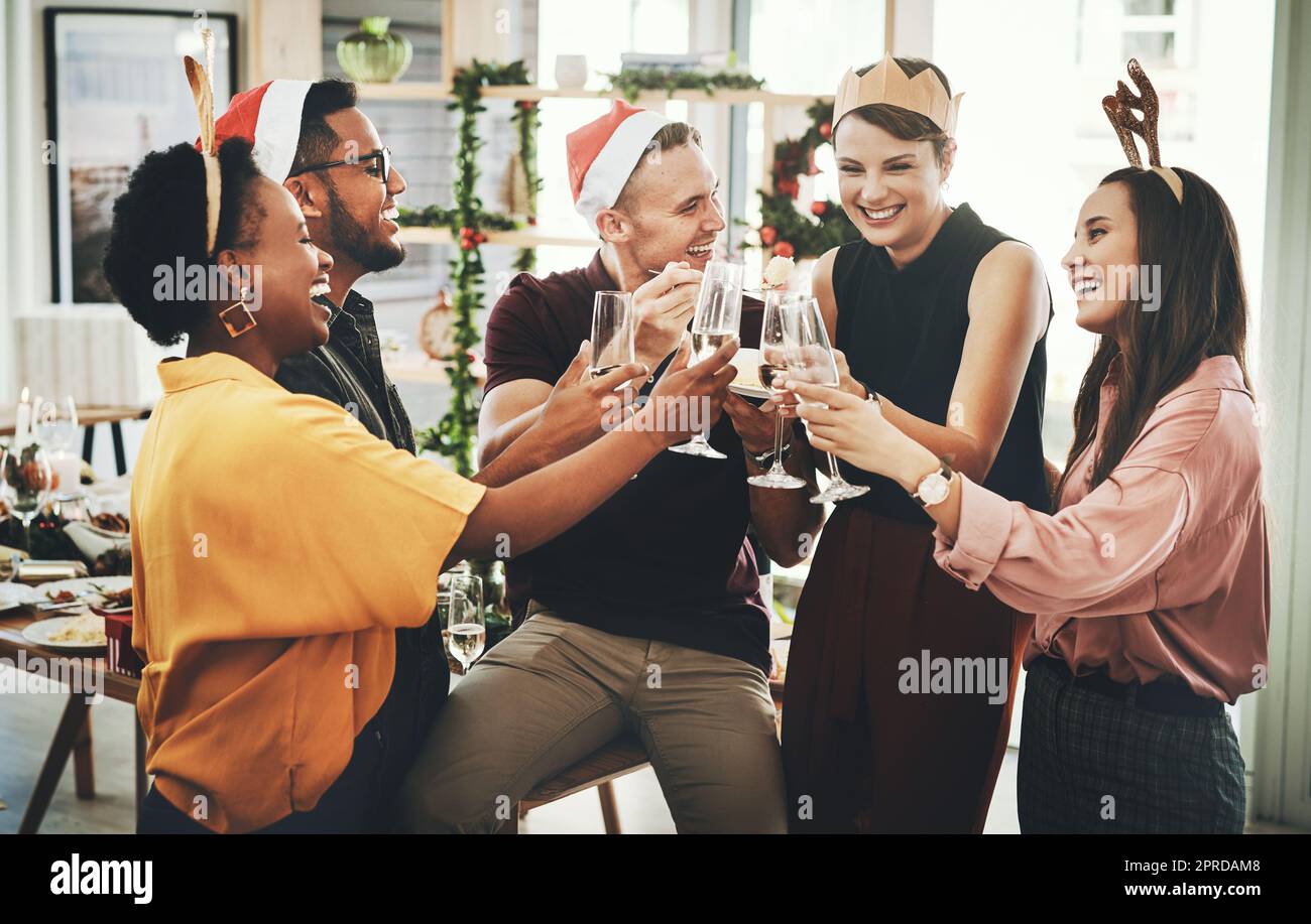 Es ist die glücklichste Jahreszeit überhaupt. Eine Gruppe von fröhlichen jungen Freunden, die anstoßen, während sie Weihnachten gemeinsam zu Hause feiern. Stockfoto