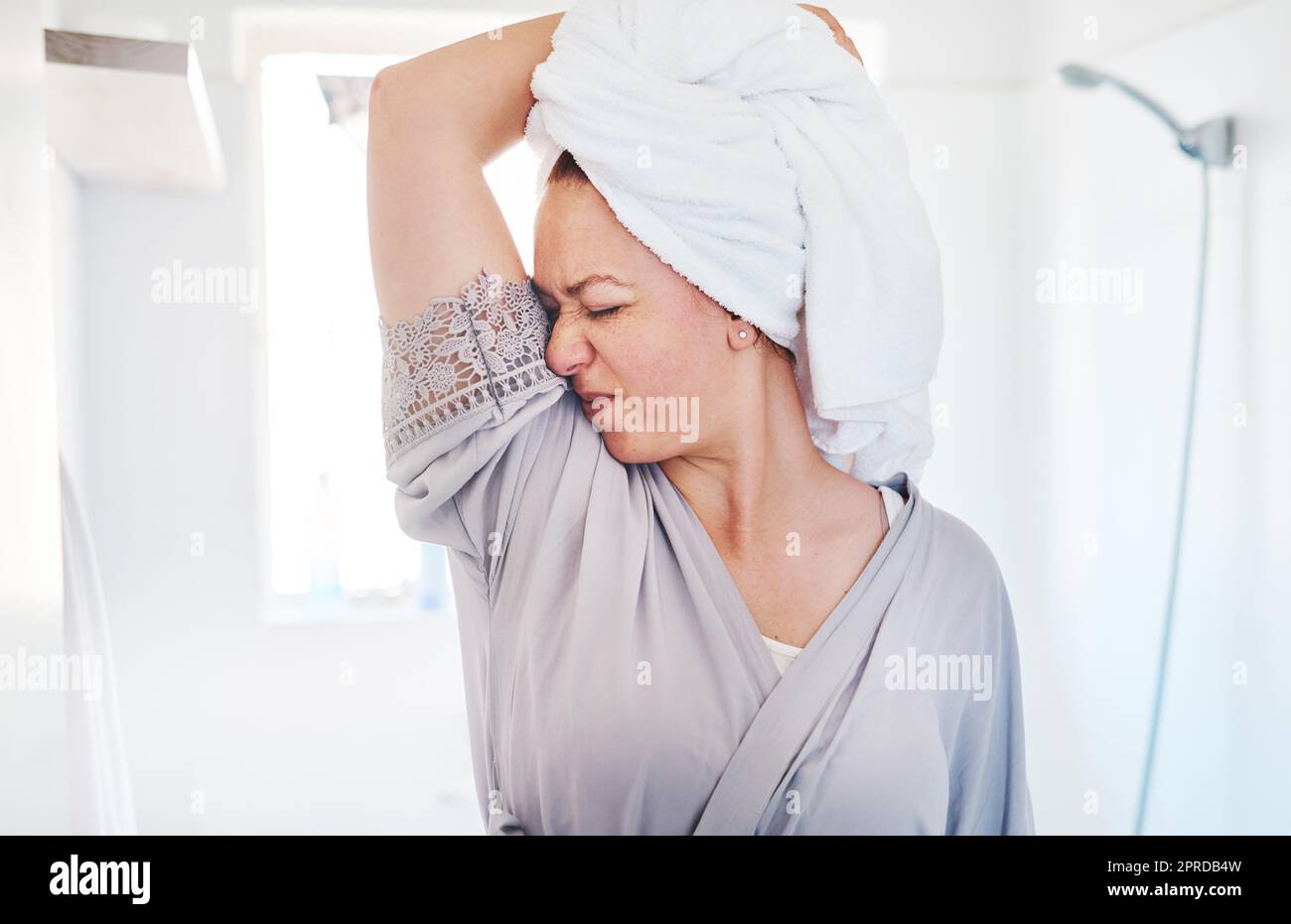 Woher kommt dieser Geruch? Eine junge Frau riecht an ihren Achselhöhlen. Stockfoto