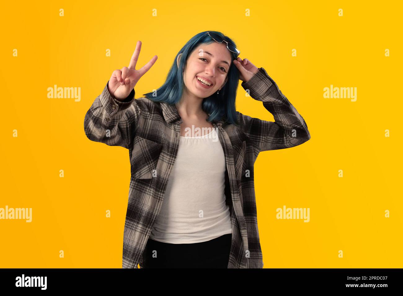 Lächelnde junge Studentin mit blauem Haar, die positive Gesten macht, mit isolierten Händen auf gelbem Hintergrund Stockfoto