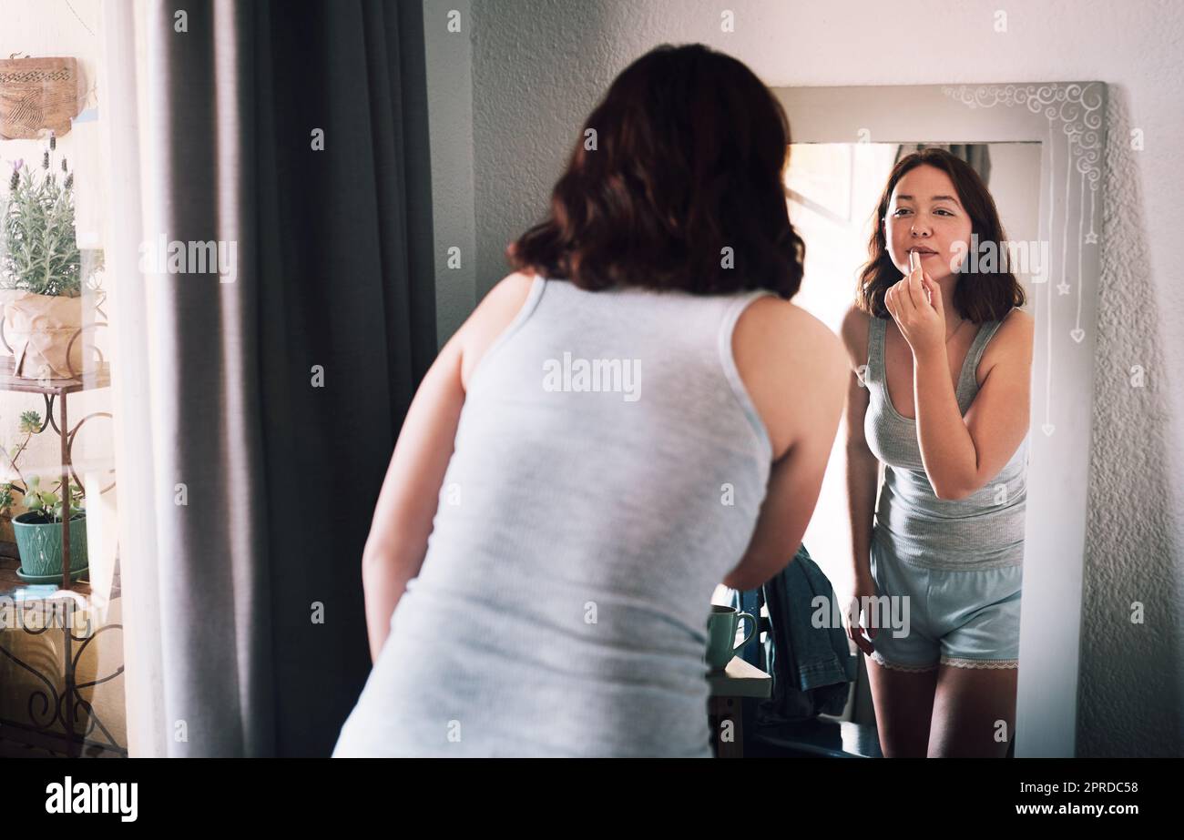 Mal sehen, wie meine Lippen darin aussehen. Eine attraktive junge Frau, die Lippenstift aufbringt, während sie zu Hause vor dem Spiegel in ihrem Schlafzimmer steht. Stockfoto