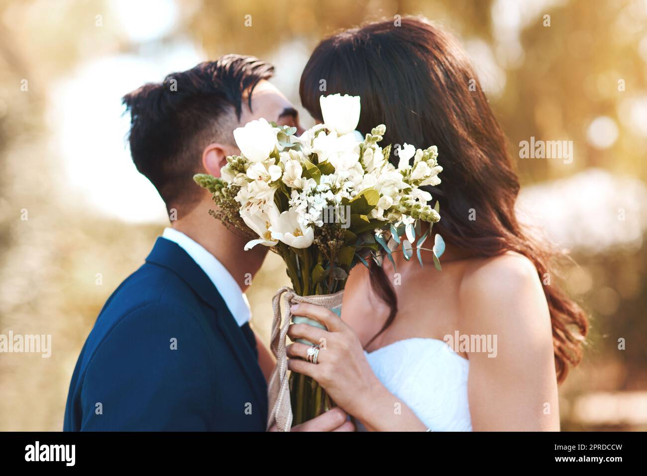 Waren bereit für diese Flitterwochen. Eine Braut und ein Bräutigam bedeckten ihre Gesichter mit einem Blumenstrauß beim Küssen. Stockfoto