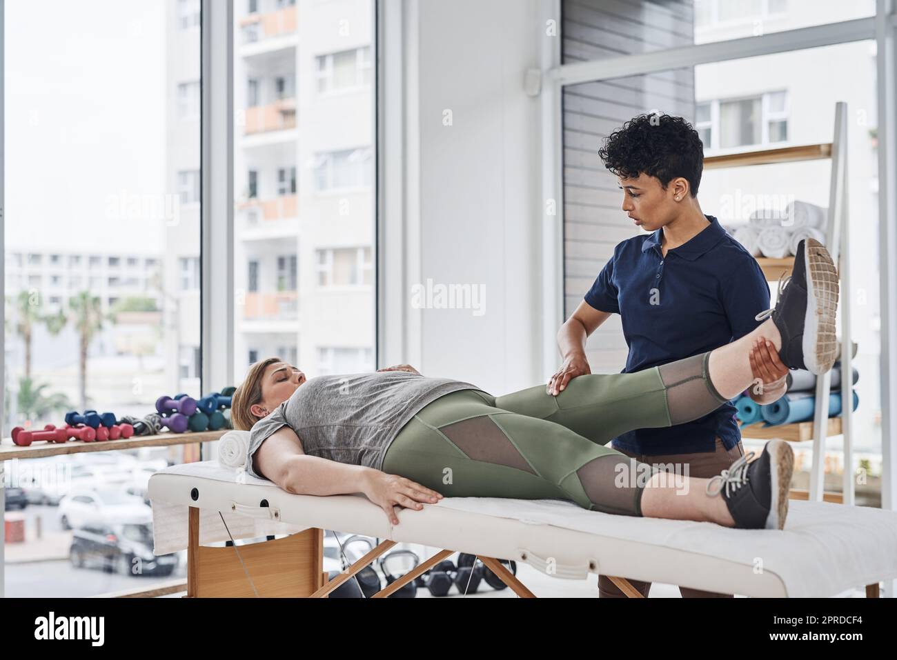 Eine junge Physiotherapeutin macht mit ihrer Patientin in ihrem Büro in einer Klinik Beinübungen. Stockfoto