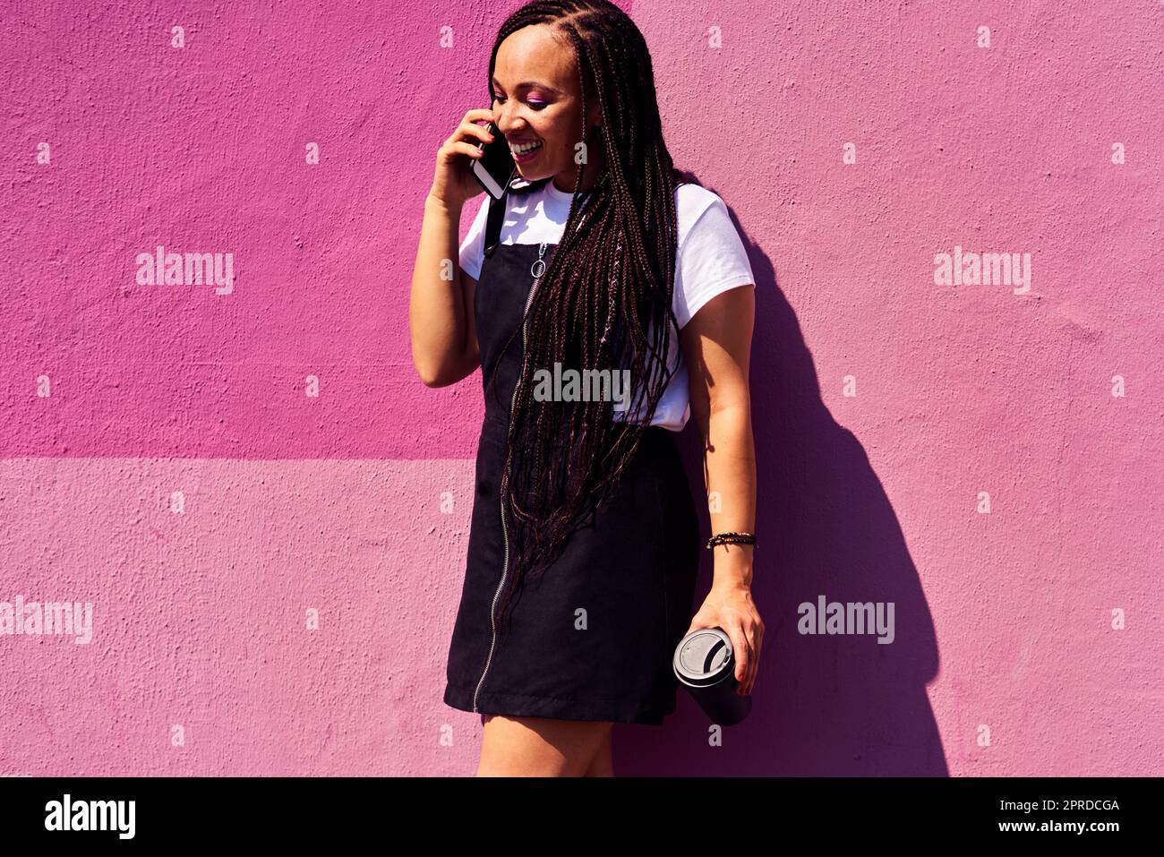 Mit der Technologie ist es so einfach, in Kontakt zu bleiben. Eine attraktive junge Frau, die allein an einer rosa Wand steht und auf ihrem Handy spricht. Stockfoto
