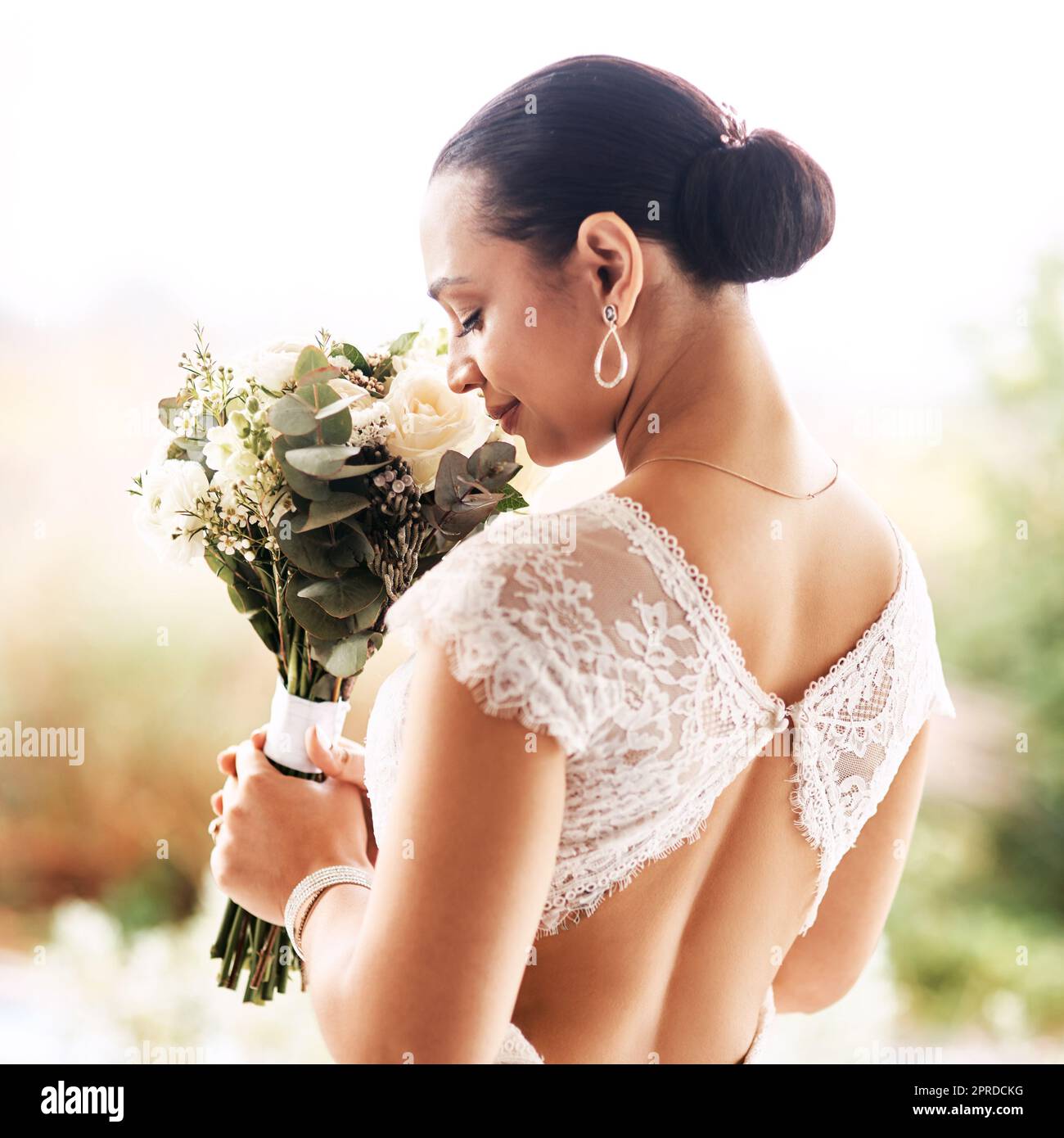 Der Duft der Liebe. Eine schöne junge Braut riecht an ihrem Hochzeitstag im Freien nach ihrem Blumenstrauß. Stockfoto