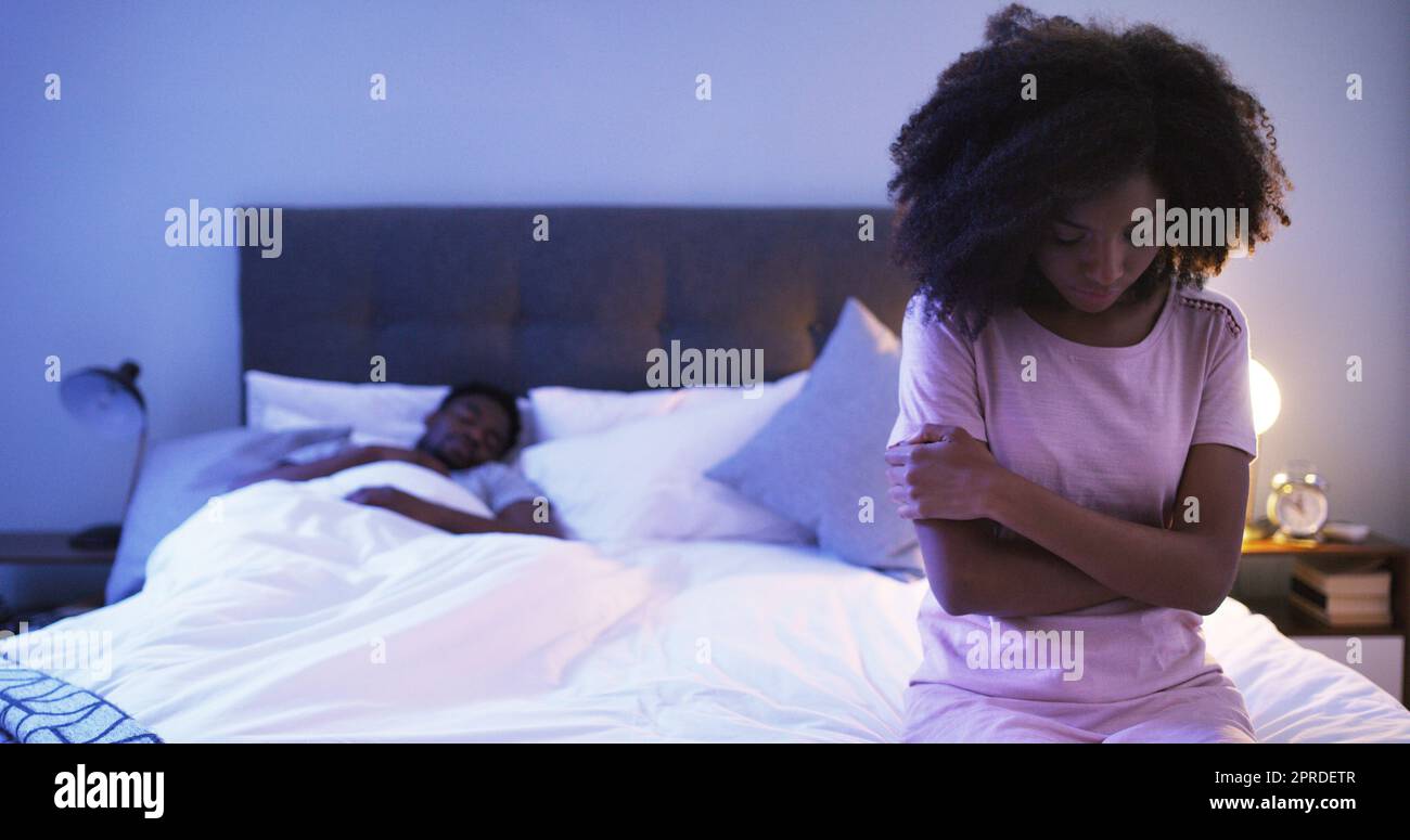 Waren in einer Beziehung, aber ich fühle mich so allein. Eine besorgt aussehende junge Frau auf einem Bett mit ihrem Mann im Hintergrund schlafen sitzen. Stockfoto