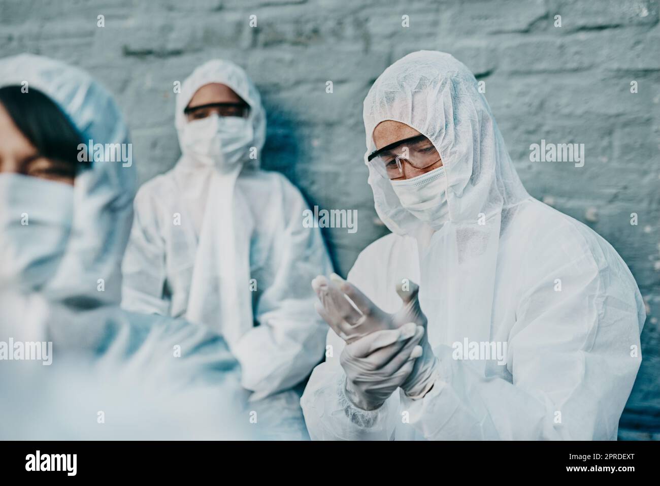 Covid-, Pandemie- und Team-Mitarbeiter im Gesundheitswesen tragen schützende psa, um die Ausbreitung des Virus an einer Quarantänestelle zu verhindern. Besorgter Ersthelfer trägt einen Schutzanzug und überprüft seinen Schutzhandschuh Stockfoto