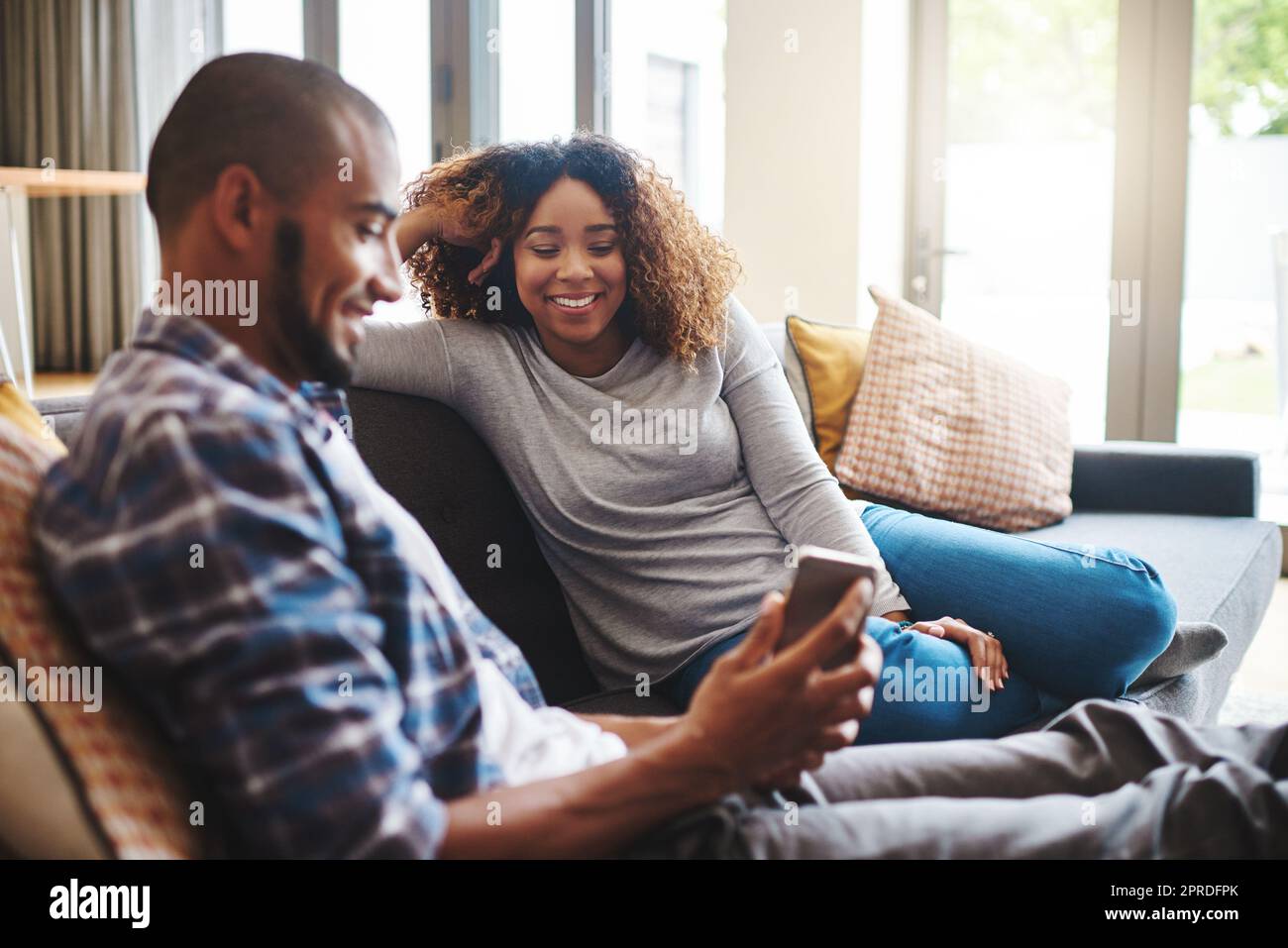 Glückliches, sorgenfreies und entspanntes Paar, das SMS auf dem Telefon liest, während es auf der Couch sitzt. Mann und Frau lächeln und lachen, während sie eine Online-App für soziale Medien durchsuchen oder zu Hause lustige Videos anschauen Stockfoto