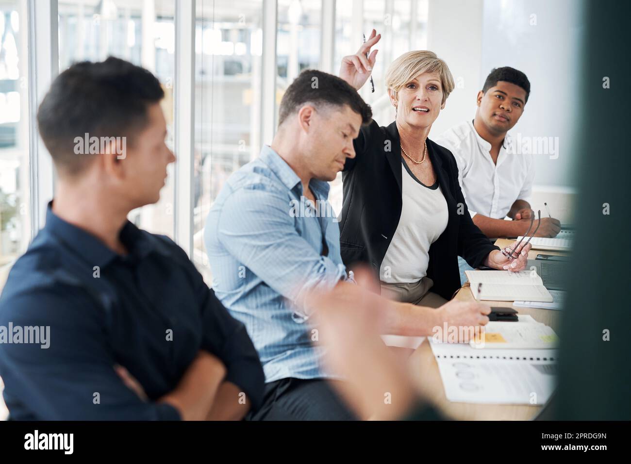Eine Frage, die eine Geschäftskonferenz auslöste. Eine reife Geschäftsfrau hob ihre Hand, um während eines Meetings Fragen zu stellen. Stockfoto