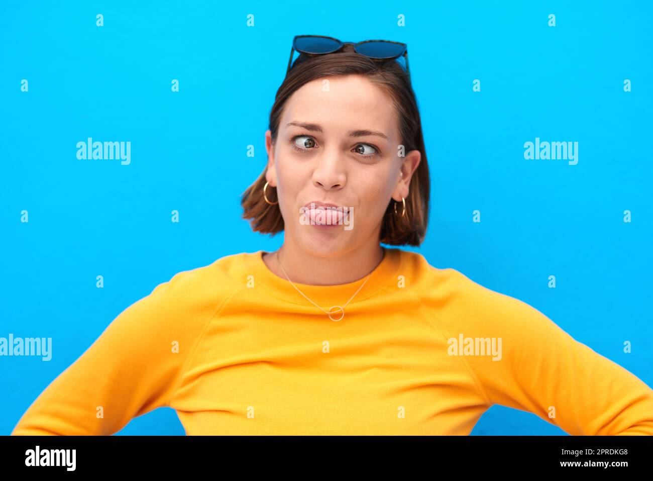 Lockere dich auf und sei albern. Eine junge Frau, die Gesichter vor blauem Hintergrund macht. Stockfoto