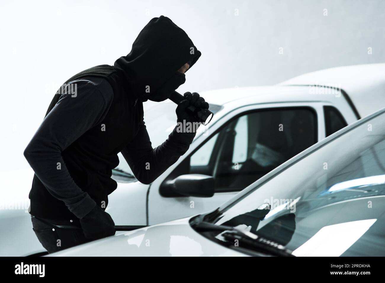 Der Raubtier auf dem Parkplatz. Ein maskierter Verbrecher, der mit einer Taschenlampe in ein leeres Auto auf einem Parkplatz schaut. Stockfoto