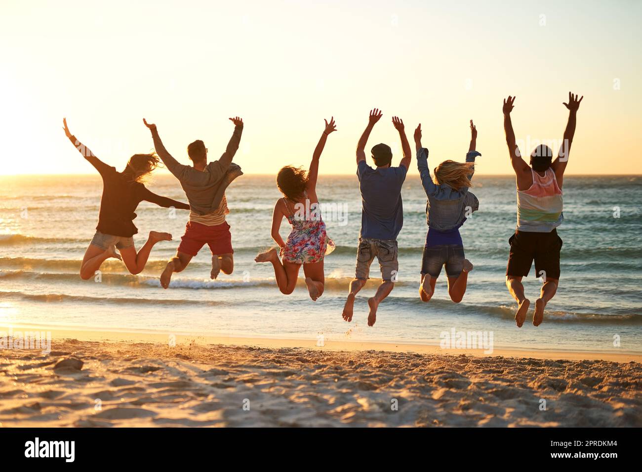 Springt und lasst euch vom Meer befreien. Rückansicht einer Gruppe junger Freunde, die am Strand in die Luft springen. Stockfoto