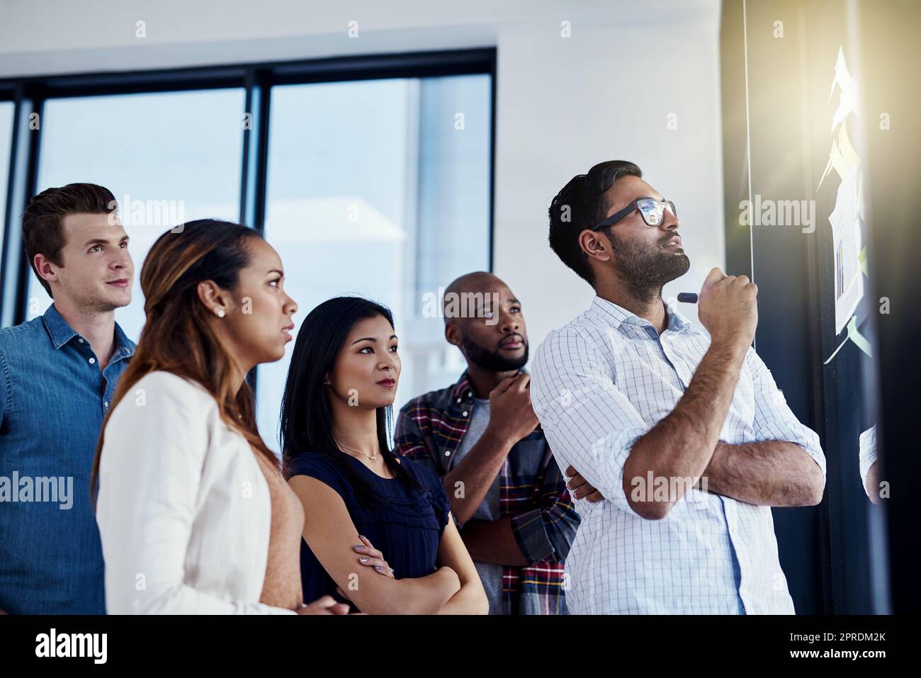 Sie kommen mit dem perfekten Plan. Ein junger Geschäftsmann, der seinen Kollegen in einem modernen Büro eine Demonstration an einer Glaswand vorführt. Stockfoto