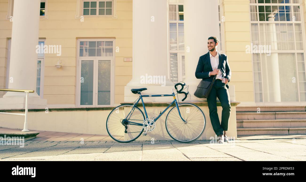 Er wird heute seinen positiven Geist im ganzen Büro verbreiten. Ein Foto eines gutaussehenden jungen Geschäftsmannes, der sich neben einem Fahrrad in der Stadt posiert. Stockfoto