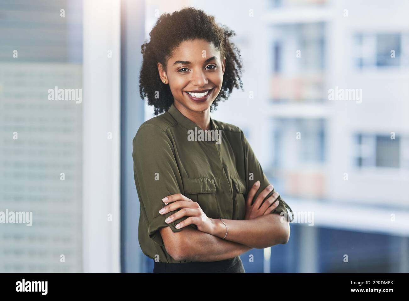 Sie alle lächeln, jede Stunde der Schicht. Porträt einer selbstbewussten jungen Geschäftsfrau, die mit gefalteten Armen in ihrem Büro steht. Stockfoto