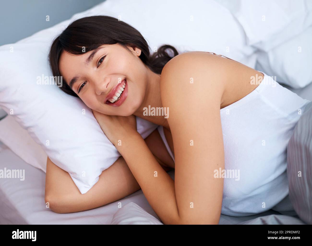 Aufwachen mit einem Lächeln. Eine fröhliche attraktive junge Frau, die morgens zu Hause in ihrem Bett schläft. Stockfoto