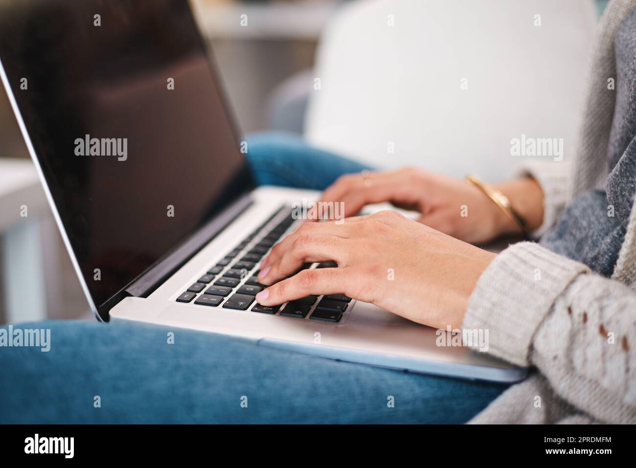 Ich bin fast fertig mit meiner Arbeit. Nahaufnahme einer unkenntlichen Frau, die tagsüber auf einem Laptop tippt, während sie zu Hause auf einem Sofa sitzt. Stockfoto