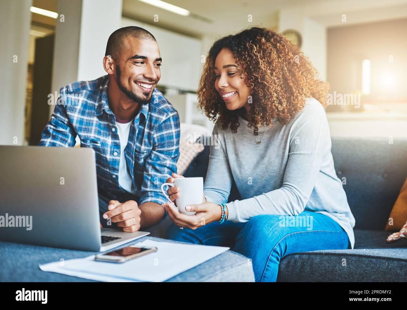 Haushaltsfinanzierung, Ersparnisse und Investitionen mit einem jungen Paar, das in seinem Wohnzimmer an einem Notebook arbeitet. Mann und Frau berechnen gemeinsam ein Haushaltsbudget, während sie sich entspannen und Kaffee auf dem Sofa trinken Stockfoto