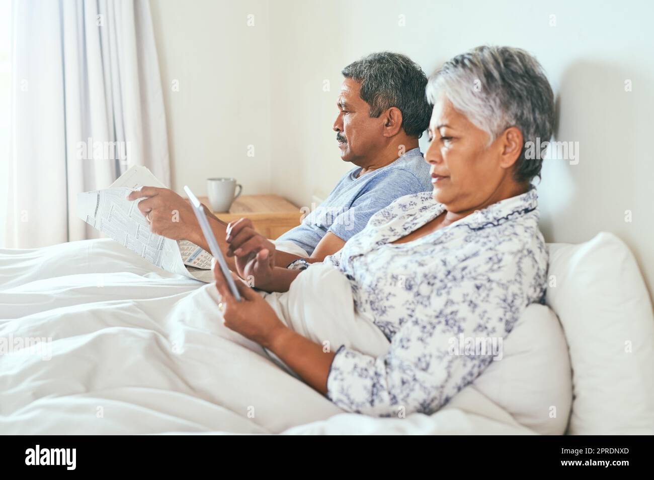 Die einfachen Dinge im Leben sind immer großartig. Ein entspanntes, reifes Paar liegt im Bett, während es morgens auf einem digitalen Tablet surft und die Zeitung zu Hause liest. Stockfoto