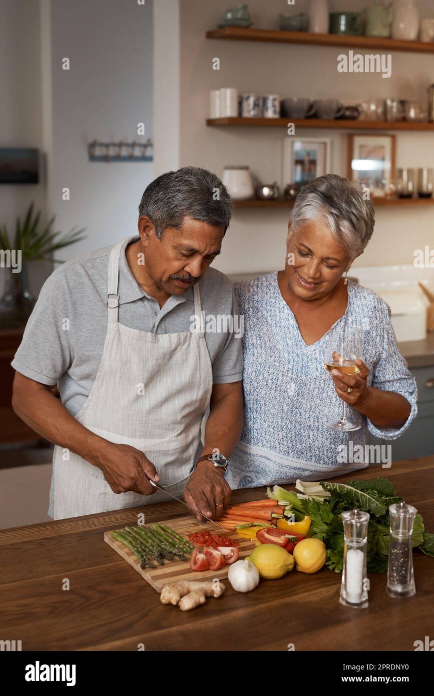 Mehr Datennächte dank Pensionierung. Ein glückliches reifes Paar trinkt Wein, während es zu Hause gemeinsam eine Mahlzeit kocht. Stockfoto