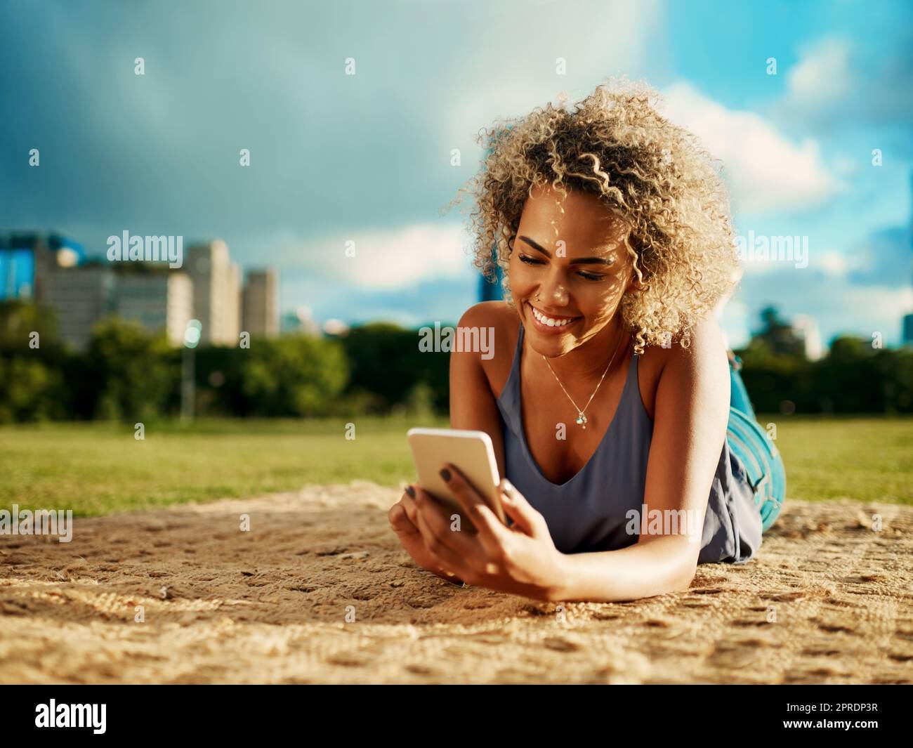 Eine attraktive junge Frau mit einem Smartphone, während sie sich in einem Park legt. Stockfoto