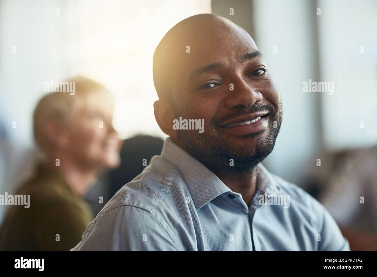 Selbstbewusster, glücklicher und motivierter Geschäftsmann, der in einem Büromeeting sitzt. Gesicht eines lächelnden afrikanischen Unternehmers, der mit seiner Jobauswahl zufrieden ist, während er an einer Präsentation oder einem Workshop teilnimmt Stockfoto